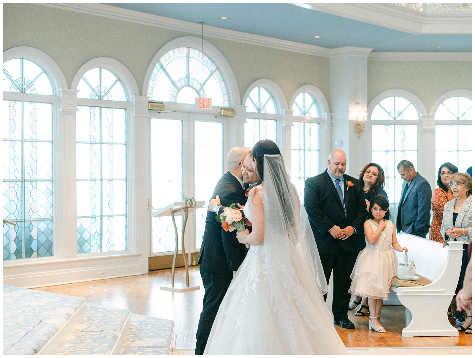Bride watches as groom and father of the bride embrace during the traditional handing over of the bride. By Elizabeth Kane Photography in Orlando Florida
