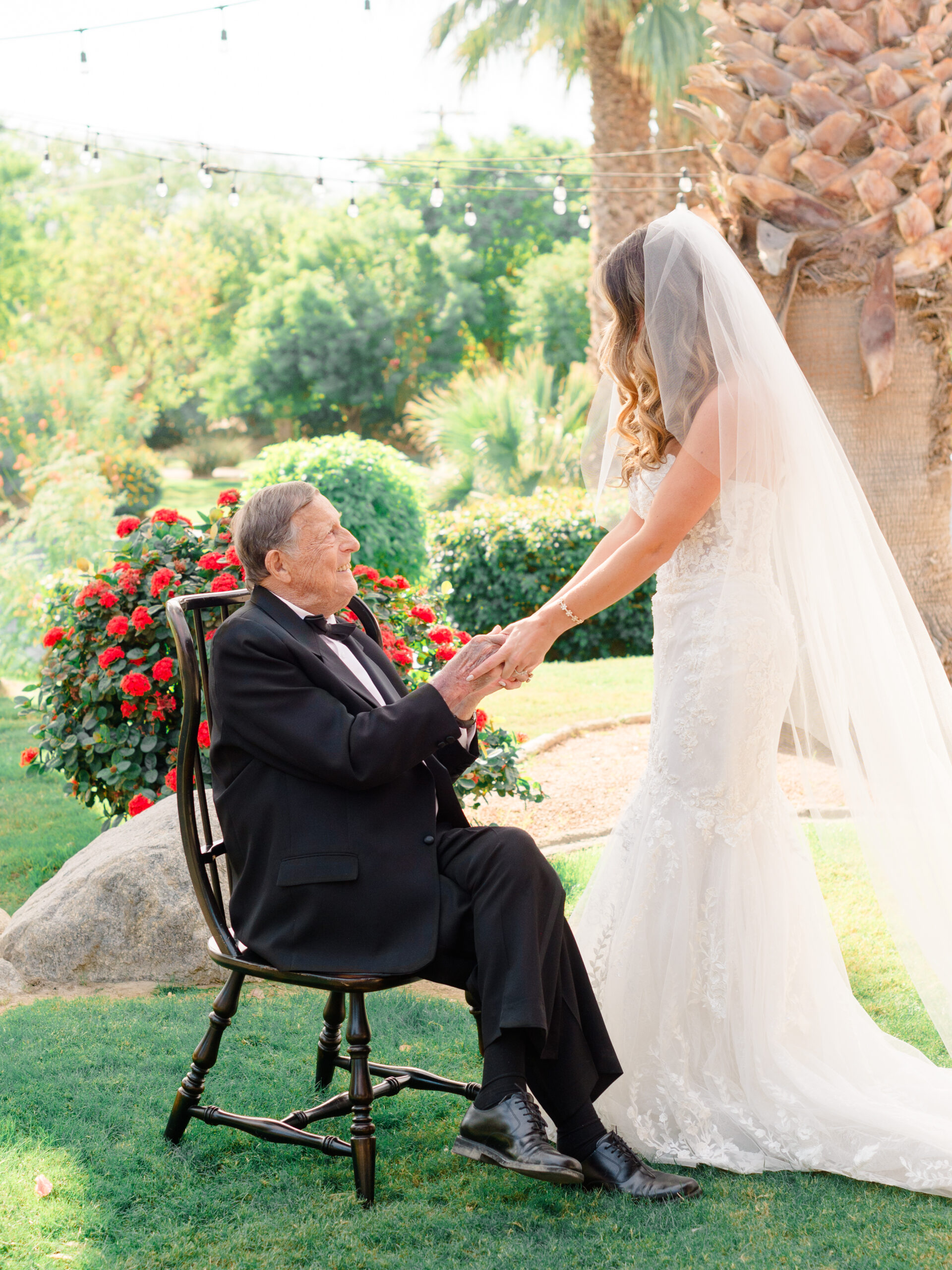 Bride sharing an emotional moment with her grandfather before the ceremony at her Bougainvillea Estate wedding in Indio, CA, surrounded by roses and palm trees.