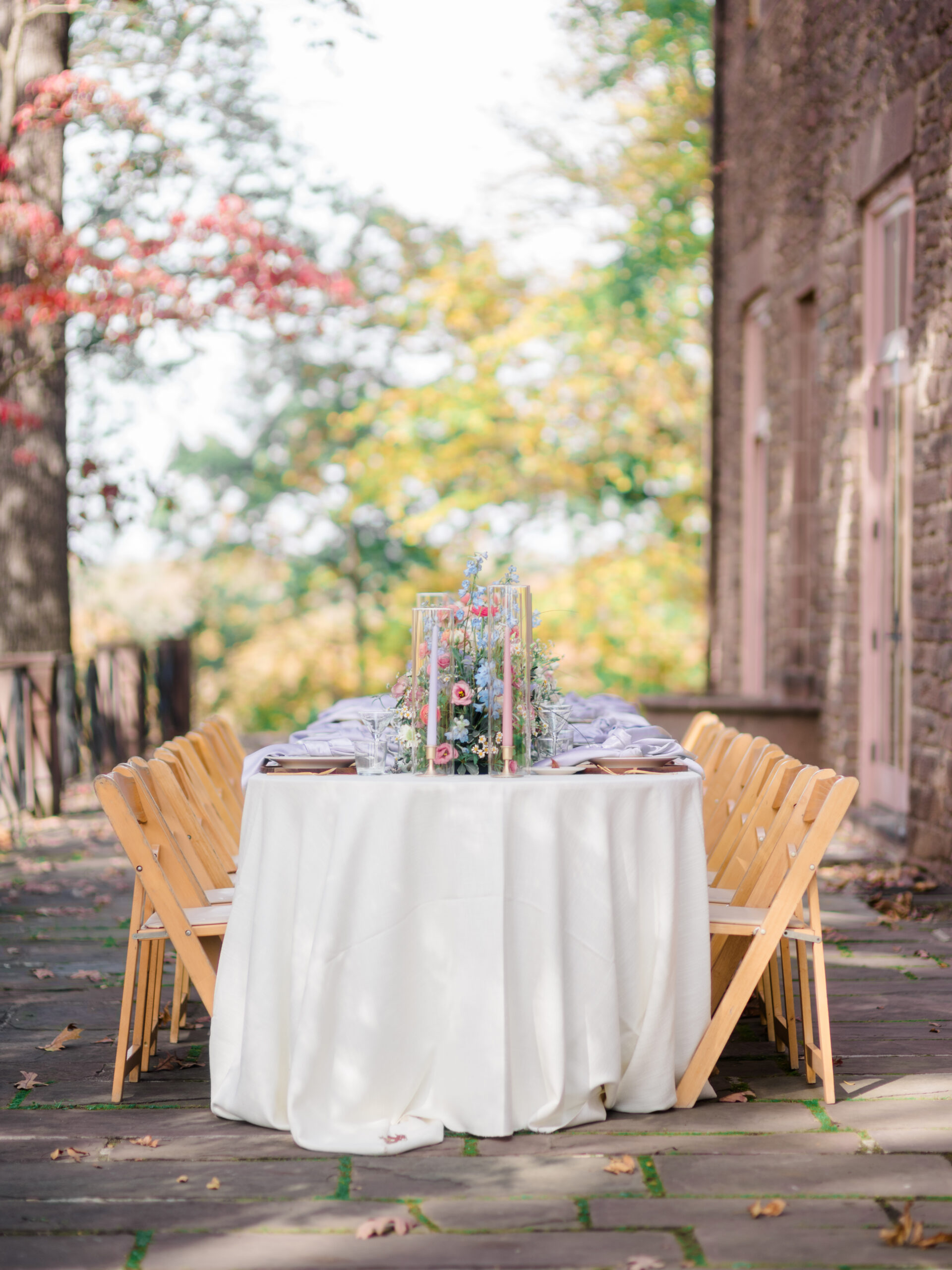 Elegant outdoor wedding table setup with pastel floral centerpiece and tall candles on a stone terrace at Tyler Gardens, captured in soft natural light as part of a bespoke wedding photography session in Philadelphia by Elizabeth Kane Photography.
