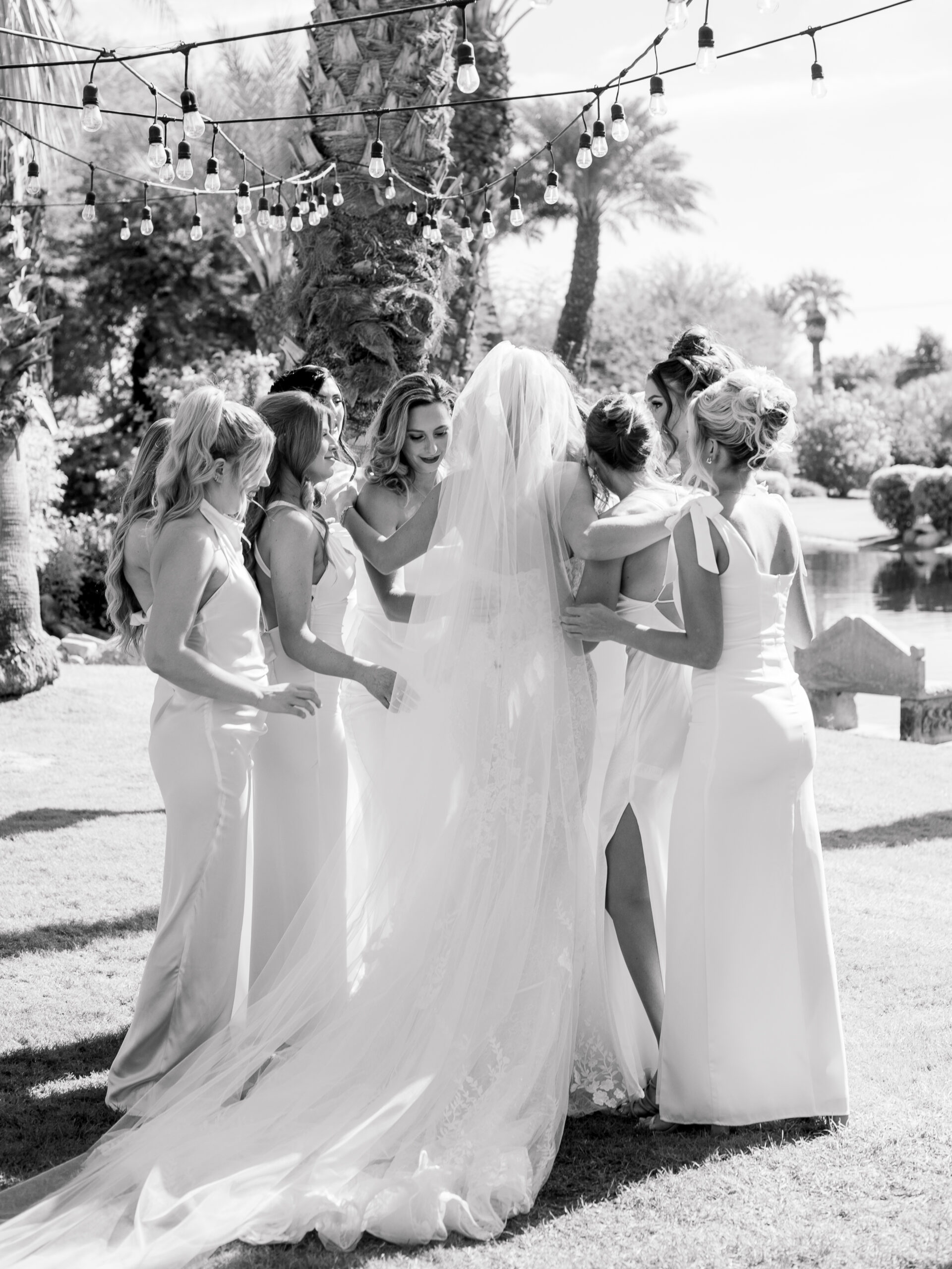 Black and white photo of bride sharing an emotional moment with her bridesmaids under string lights at her Bougainvillea Estate wedding in Indio, California.