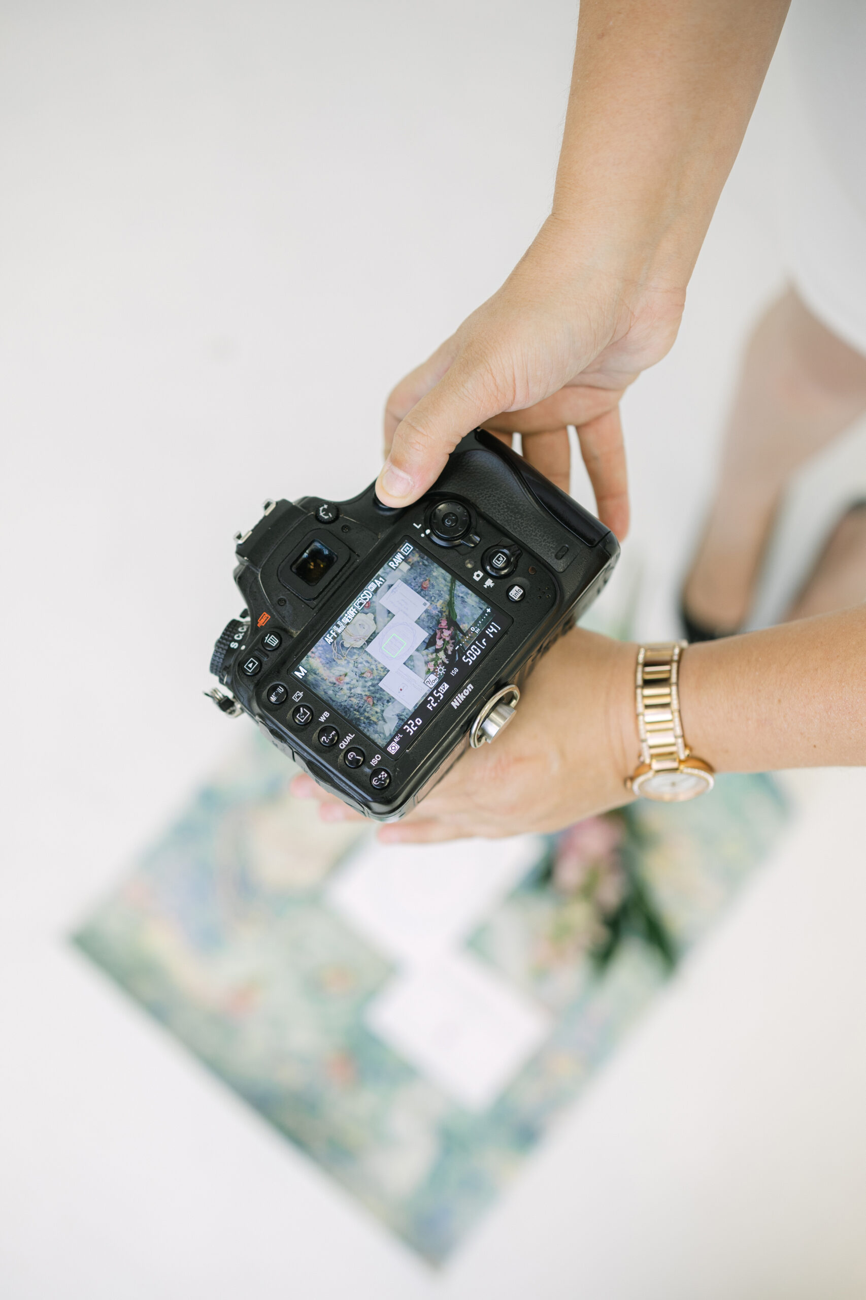 Behind-the-scenes photo of a Philadelphia wedding photographer reviewing a flatlay image on a DSLR camera, capturing details during a styled content shoot.