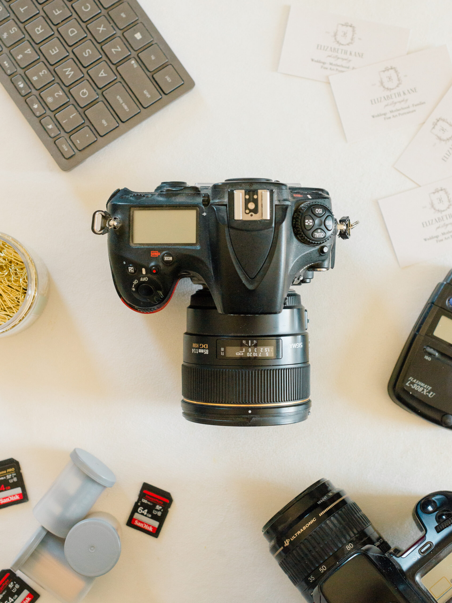 Flatlay of photography gear and branded business cards, including cameras, SD cards, and film canisters, packed for a Philadelphia wedding photography trip.