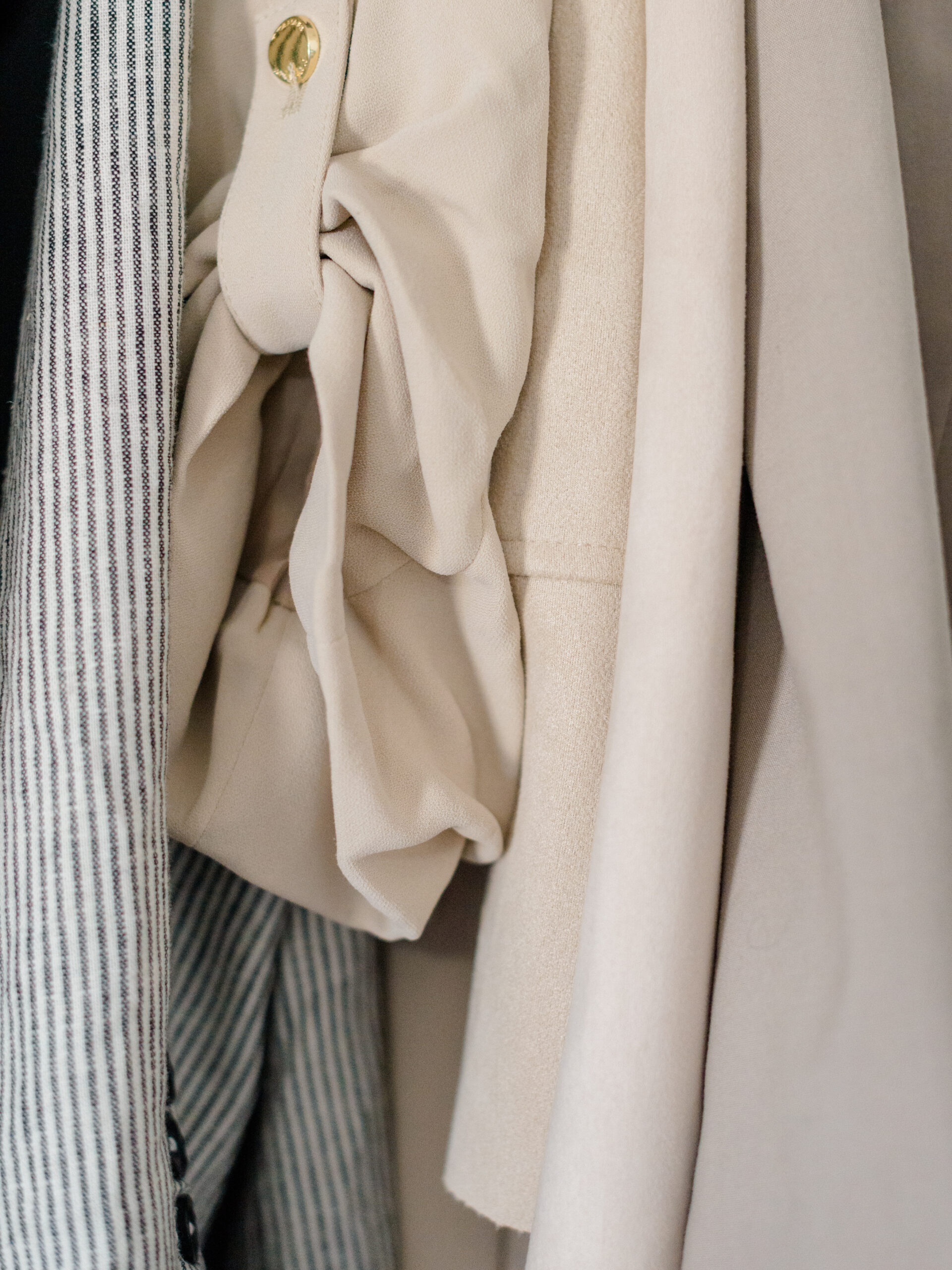 Close-up of neutral-toned wardrobe pieces, including a tailored jacket and feminine blouse, carefully styled and packed for a Philadelphia wedding photography trip.