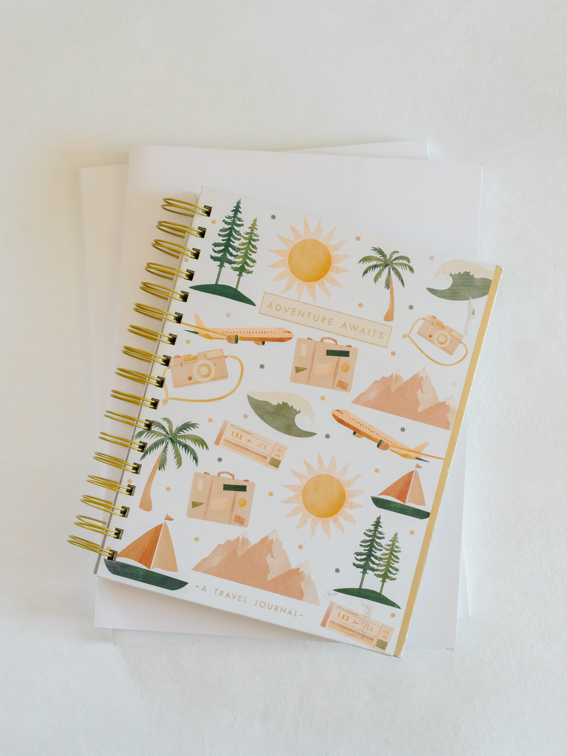 Flatlay of a spiral-bound travel journal with illustrated icons and the phrase “Adventure Awaits,” packed for a Philadelphia wedding photography trip.