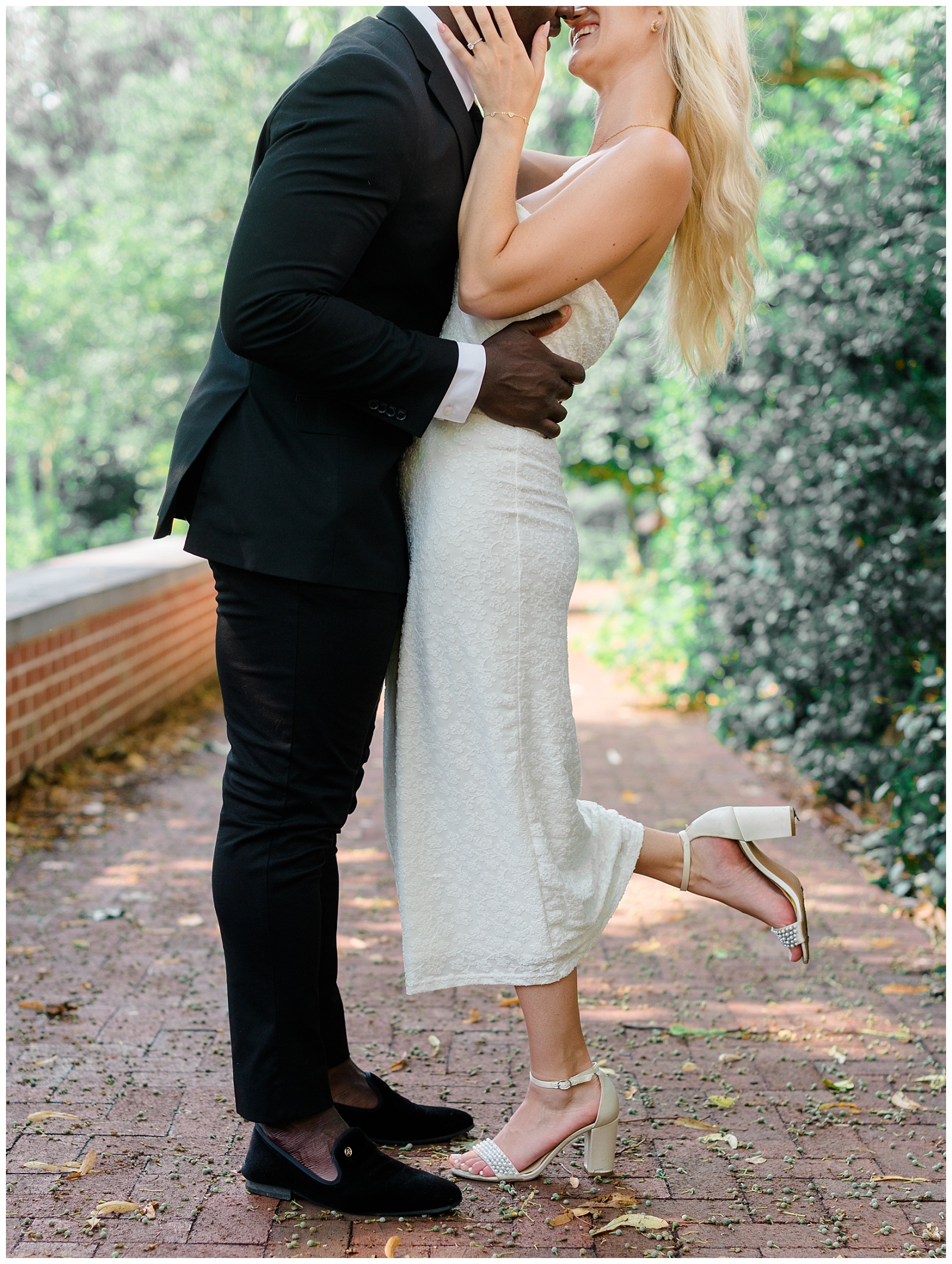 Romantic kiss during Old City Philadelphia engagement session with bride-to-be in white dress and groom-to-be in black suit, captured on a cobblestone path