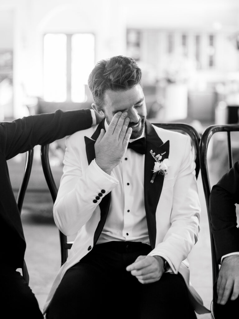 Black and white candid of a groom wiping away tears in an emotional wedding moment, showing how investing beyond the hidden costs of wedding photography preserves raw, heartfelt memories.