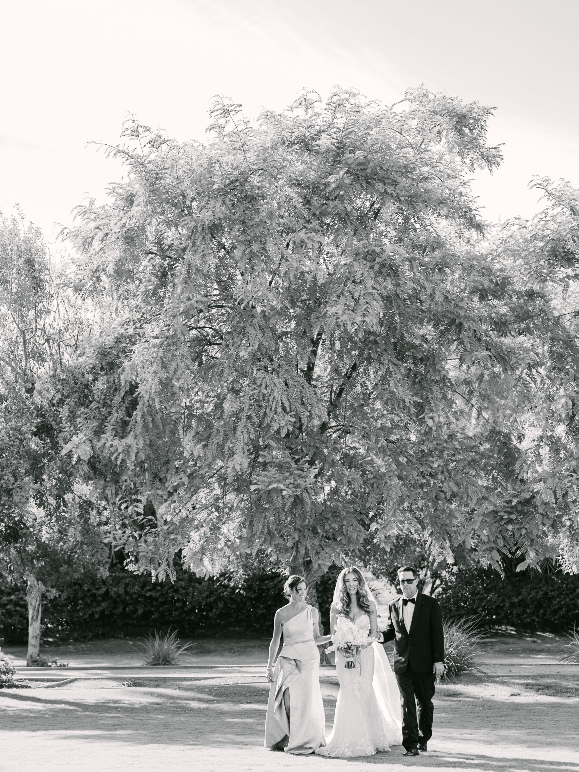 Bride walking with her parents beneath a large estate tree before the ceremony, captured as part of a calm and intentional wedding photography experience