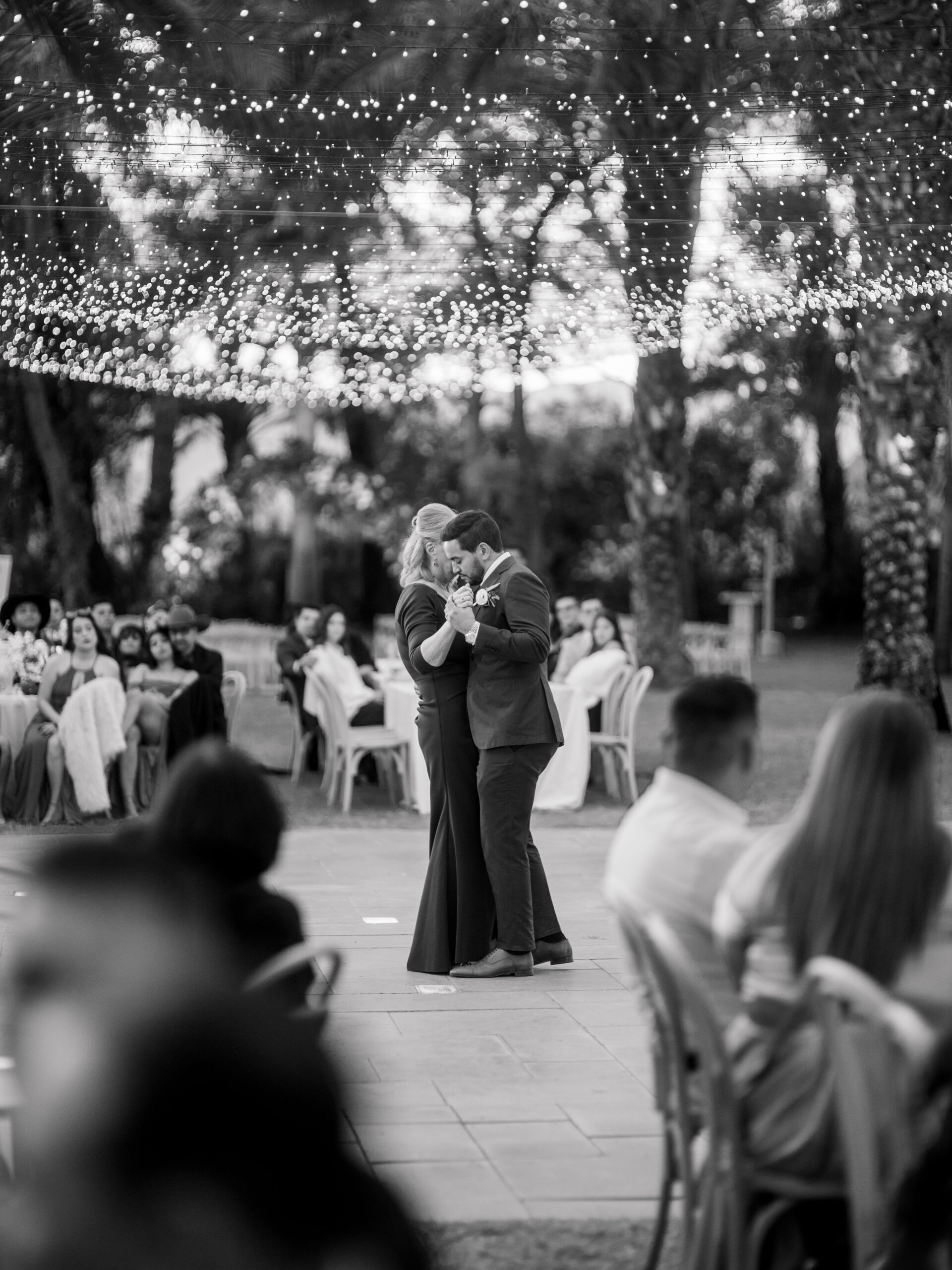 Mother and son sharing a dance beneath string lights at an outdoor wedding reception, captured as part of a calm and intentional wedding photography experience