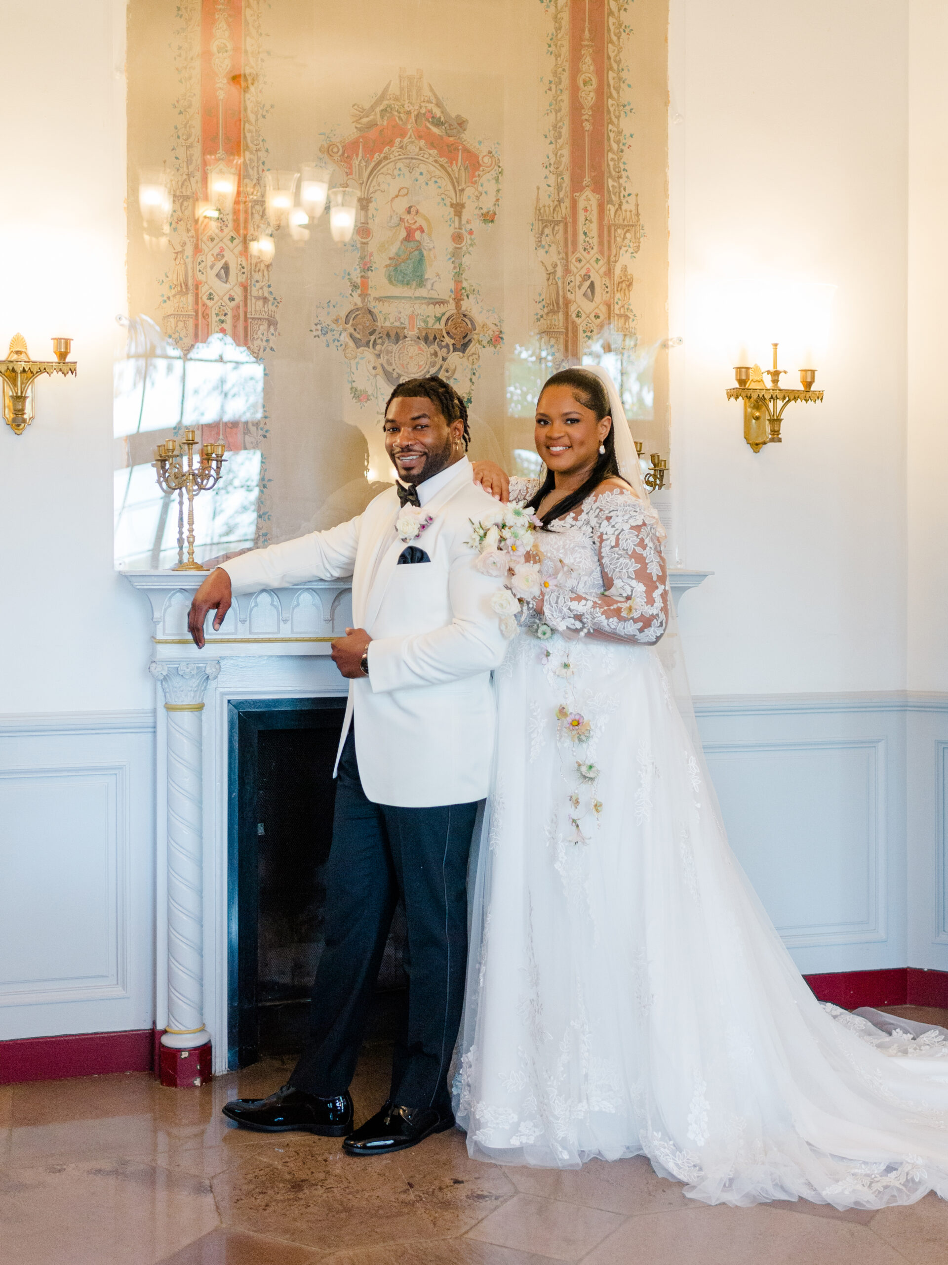 Boutique full-service wedding photography showcasing a joyful bride and groom posing together by a fireplace inside a classic estate wedding venue.